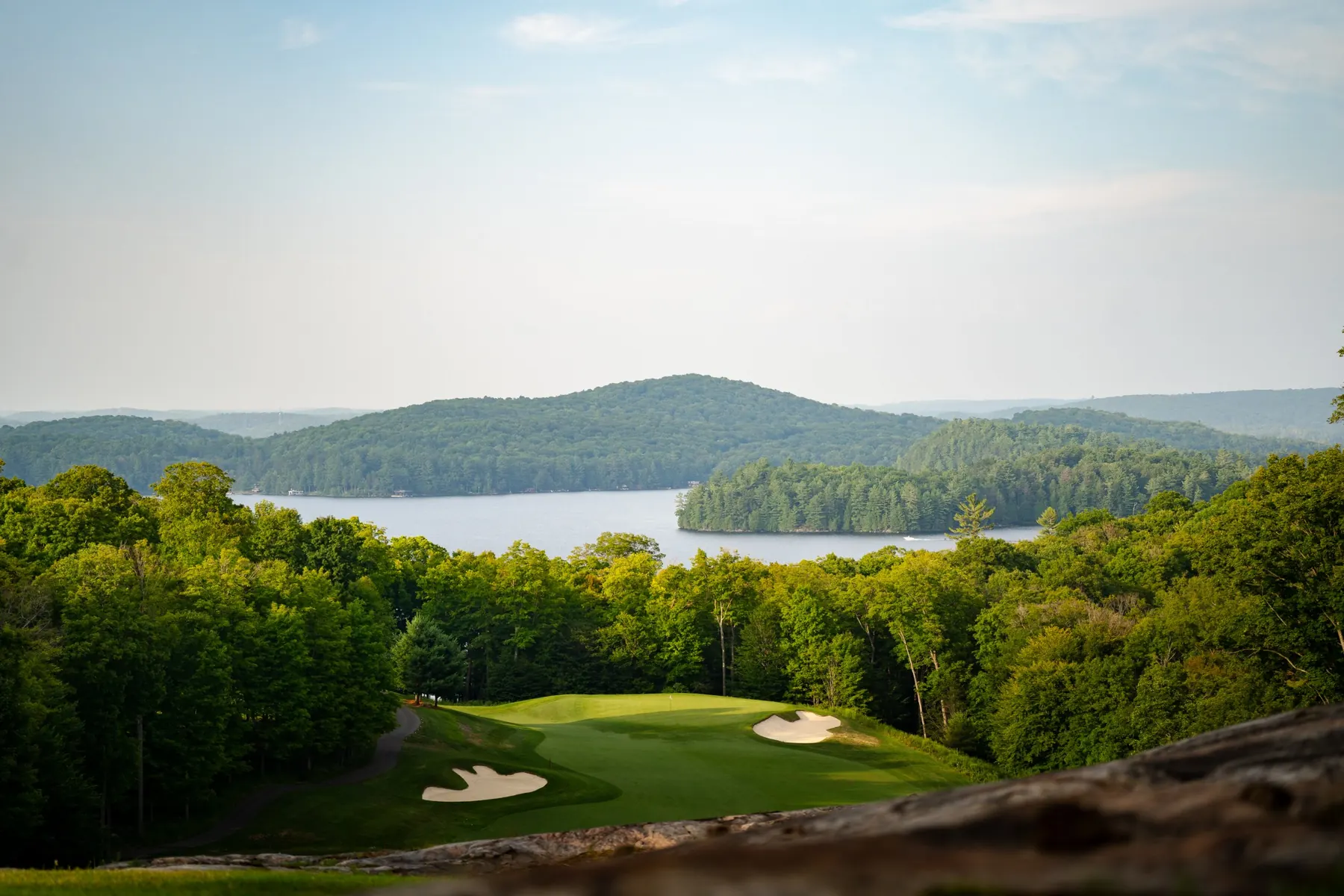A green below the island's rock outcrop, with Lake of Bays and the hills beyond