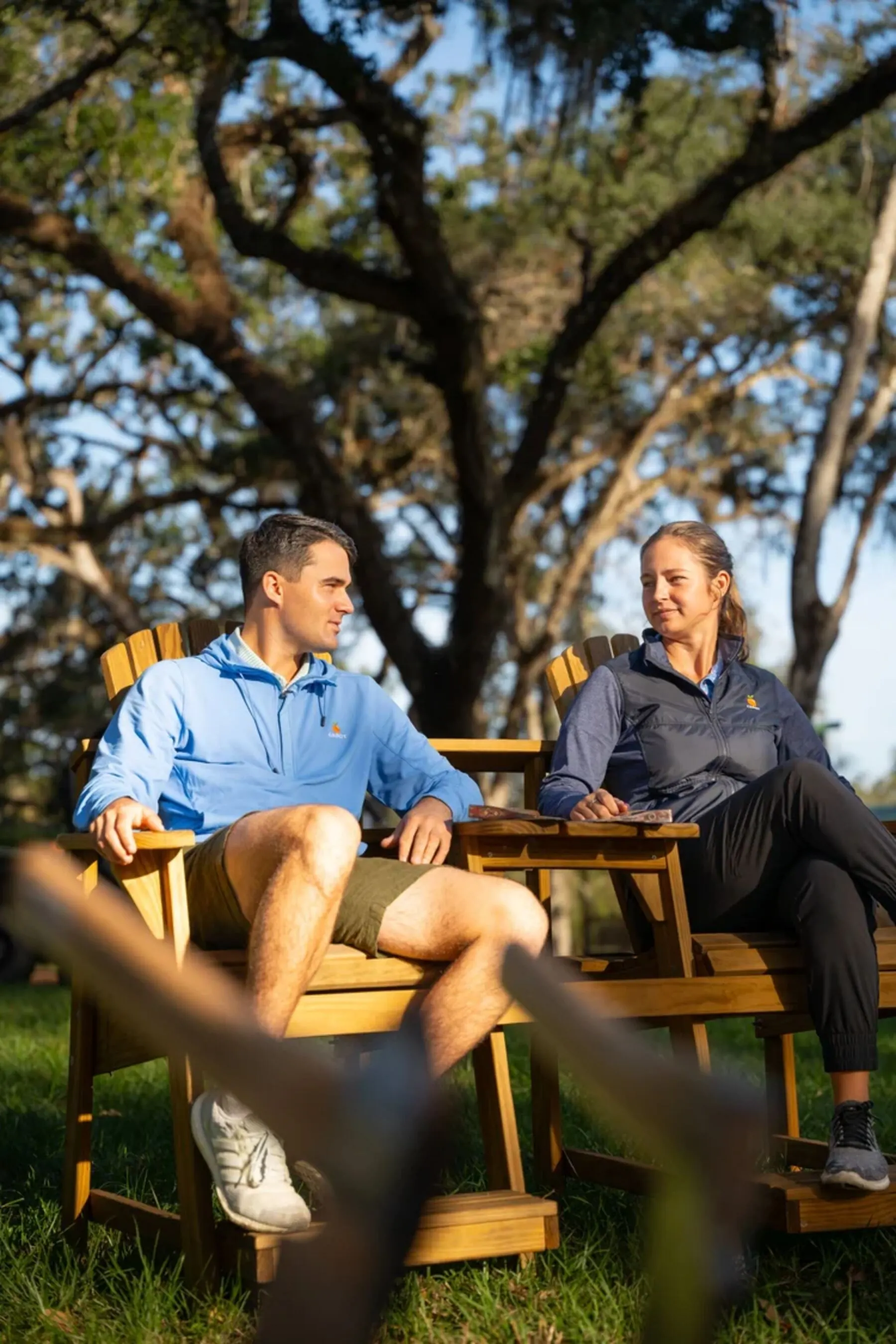 Guests relaxing in Adirondack chairs under an oak