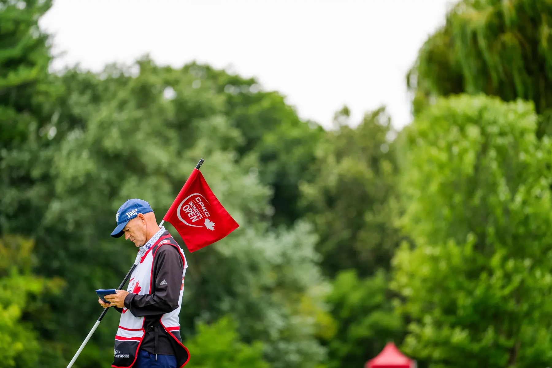 A caddie checks his yardage book holding a CPKC Women's Open flag